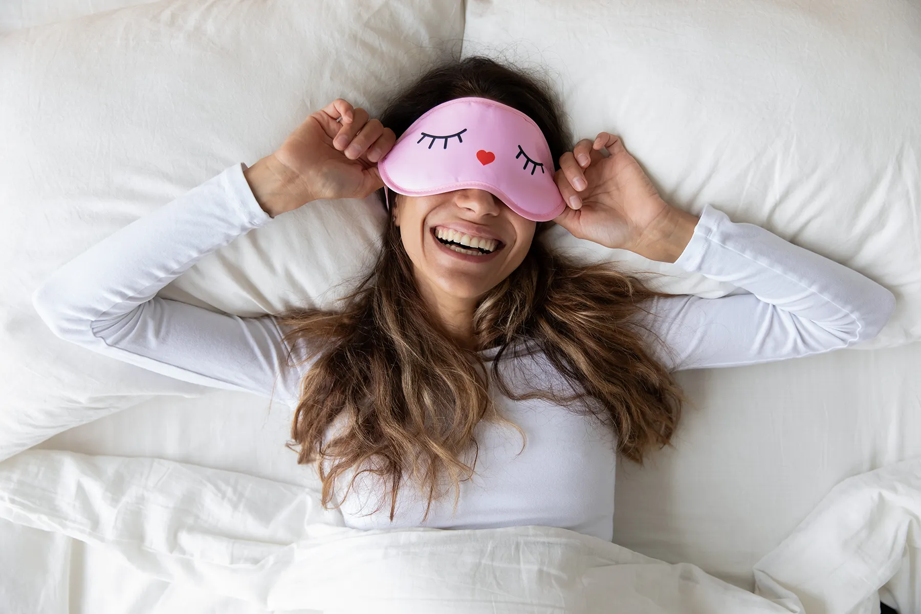Happy woman wears a sleep mask and smiles while stretching.