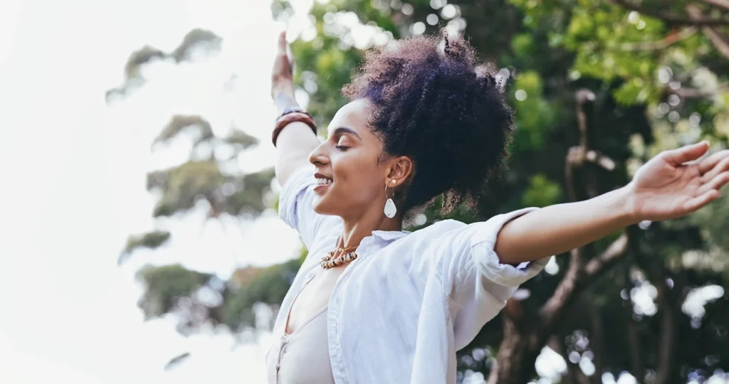 Happy Black woman stands outside with her hands outstretched as she enjoys the breeze.