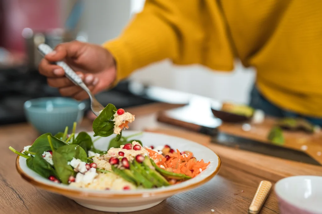 Close-up of woman eaching her fork to a heart healthy salad that has spinach, carrots, and more.