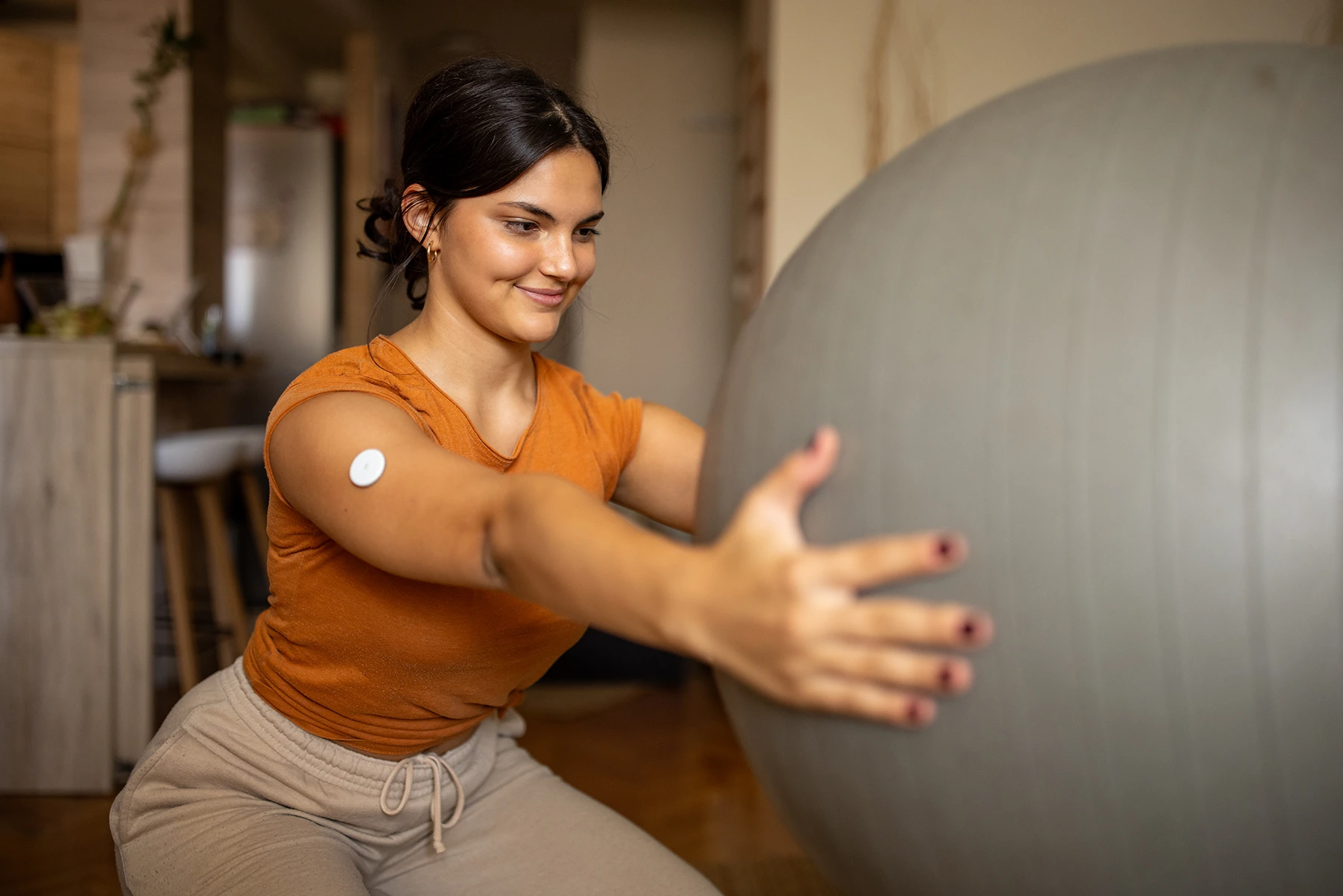 Young woman with a continual glucose monitor holds out a yoga ball as she exercises.