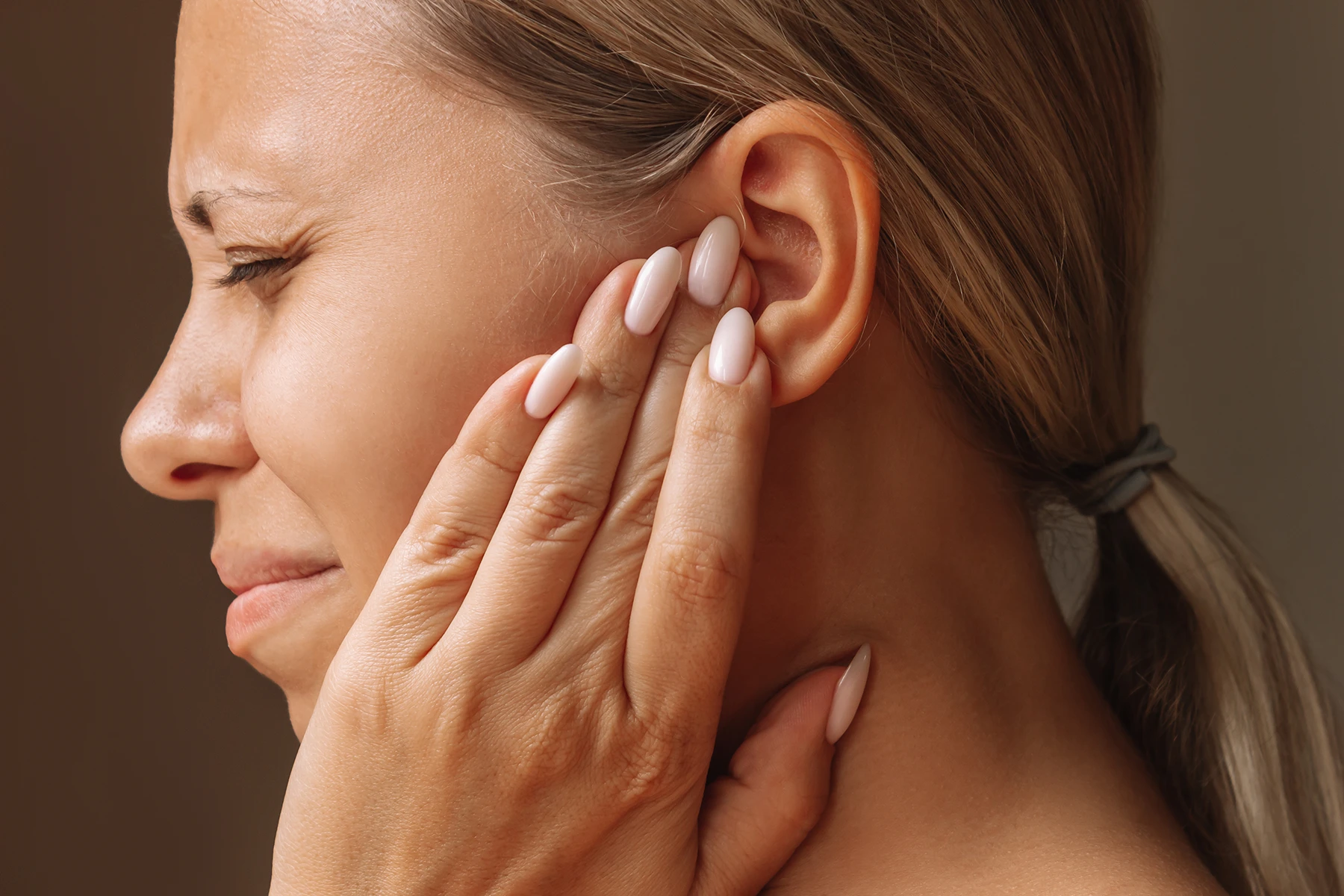 Close-up of woman holding her ear, likely due to the irriation of earwax buildup.