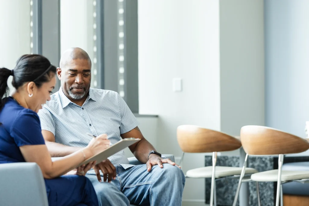 Middle aged male patient consults with young female medical professional in a hospital lobby.