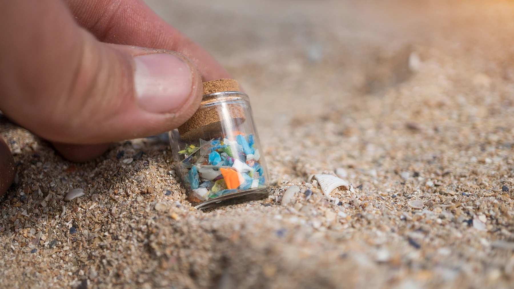 A hand holding a sample jar with tiny plastic particles collected from the need for microplastics research and its impact on health.