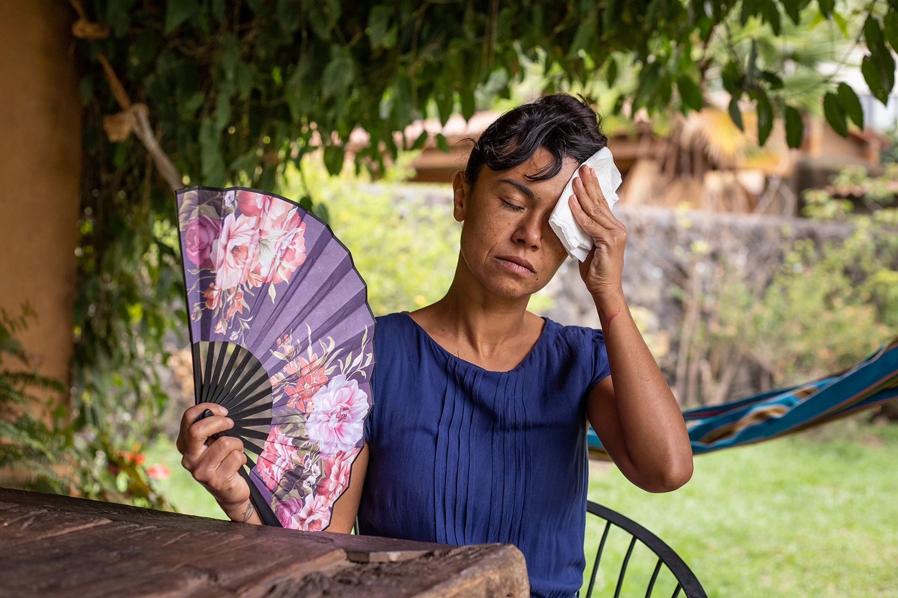 Middle-aged Hispanic woman blots at her forehead and fans her face, overheating from menopause.