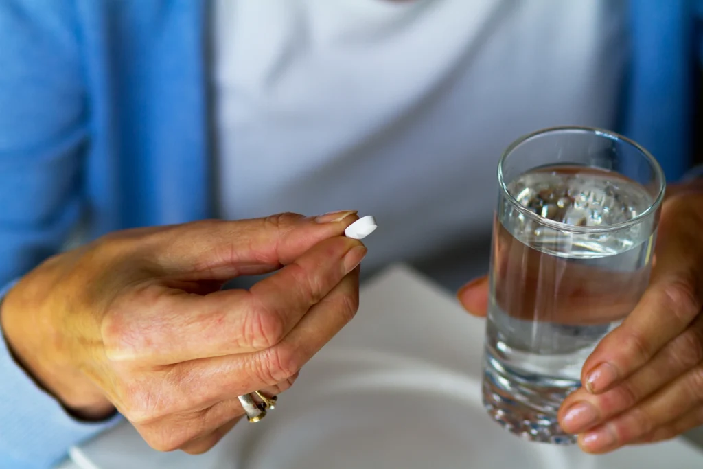 A caucasian senior woman is taking pill and is holding a glass with water. Pill is heart illness, cardiac and blood pressure.