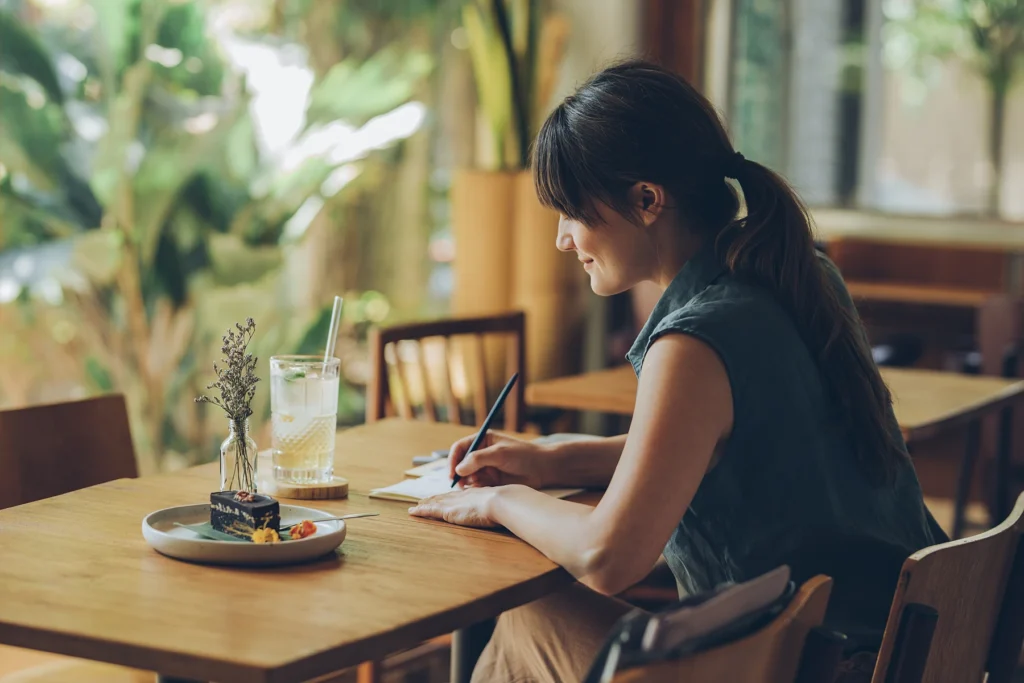 Young Woman Writing Notes in her Notebook while Sitting at a Cafe