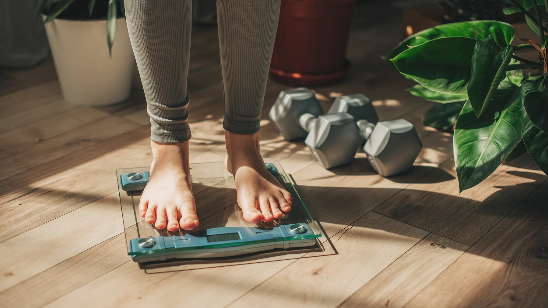 Close-up of woman's feet on scale. Hand weights are on the floor next to the scale.