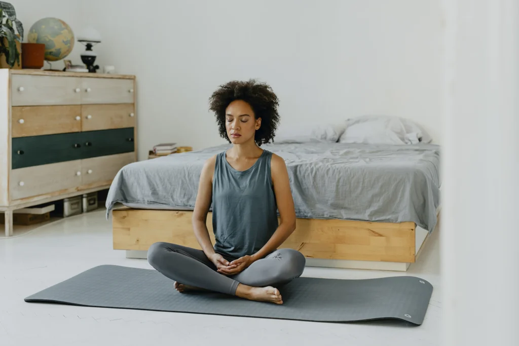 Beautiful young Black woman doing yoga practice on her bedroom floor as part of her morning ritual.