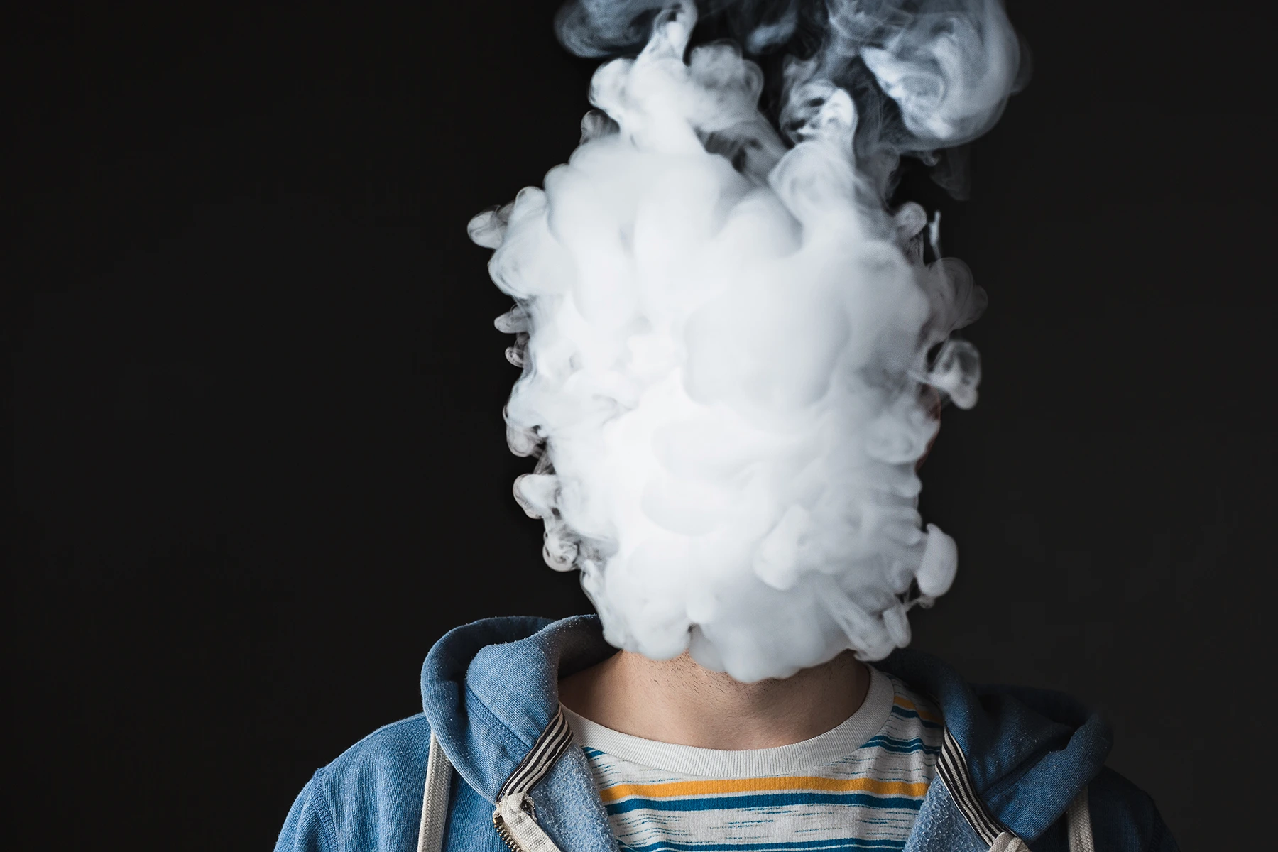 A cloud of vaping smoke covers a young boy's face. Stock image for health article.