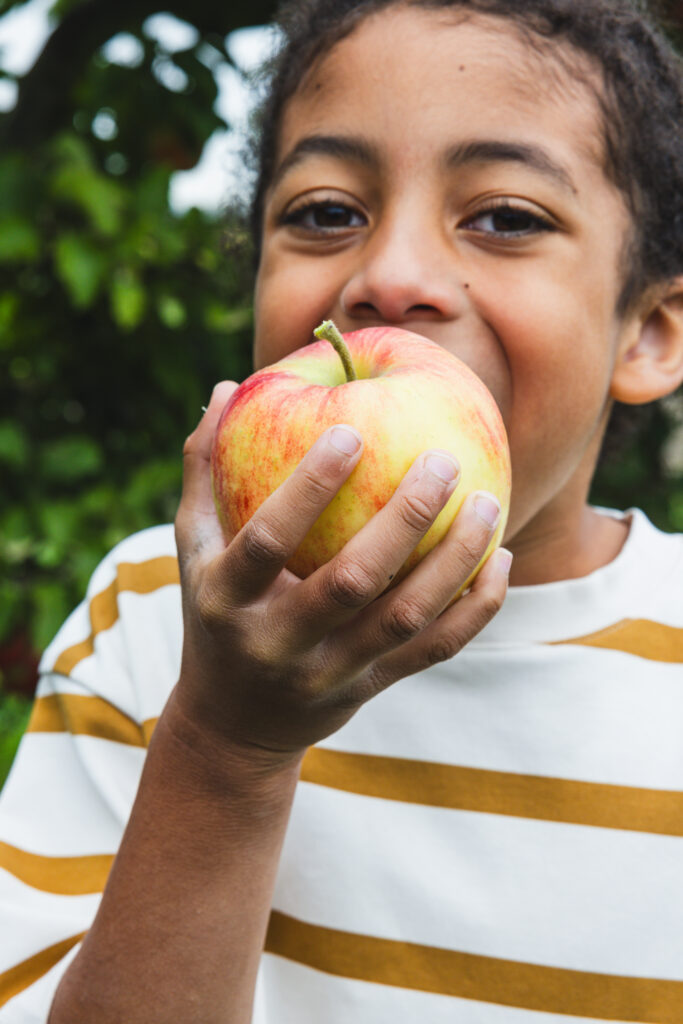 A young child gleefully biting into an apple. Part of the Sylvester Comprehensive Cancer Center Art is Medicine gallery. Photo credit: Meg Stacker King