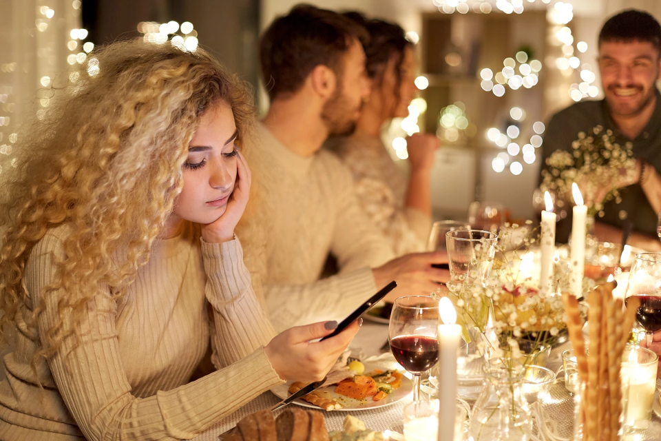 Woman at holiday dinner party is mentally drained and checking her phone.