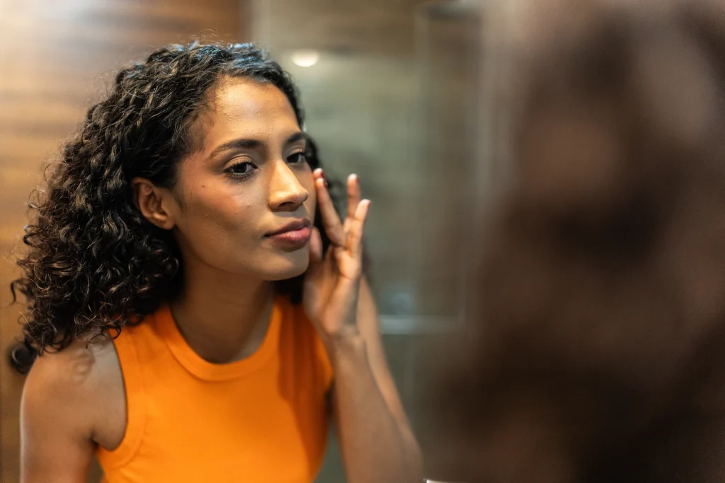 Woman of approximately perimenopause age checks the skin on her face in the bathroom at home - stock photo