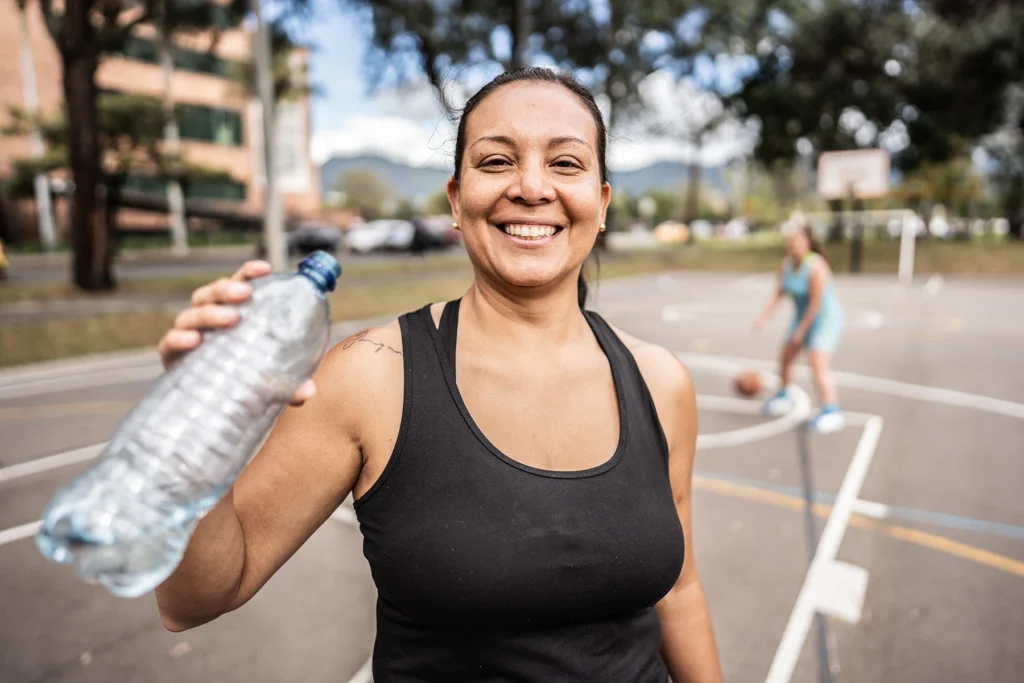 Portrait of a mature Hispanic woman drinking water outdoors while exercising - stock photo