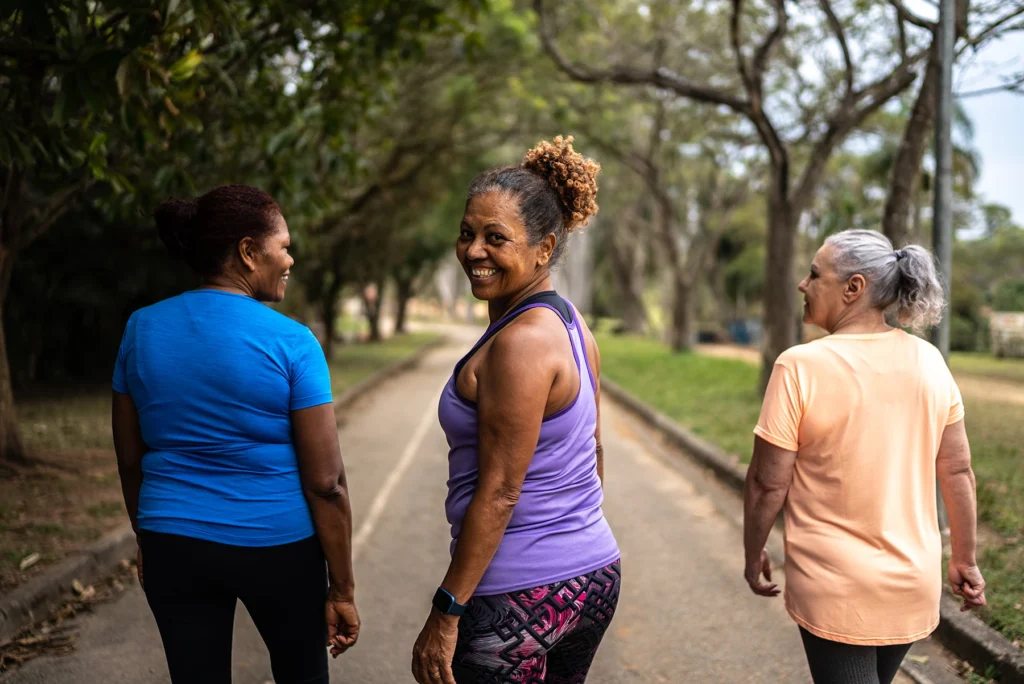 A senior woman turns and smiles while walking outside in the park with friends - stock photo