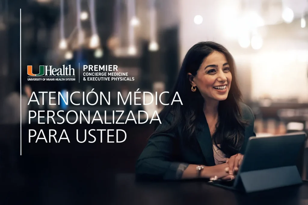 Smiling professional woman seated at a table, looking engaged with a tablet, promoting UHealth University of Miami Health System Premier Concierge Medicine and Executive Physicals, with text "Atención Médica Personalizada Para Usted" (Personalized Medical Attention for You).