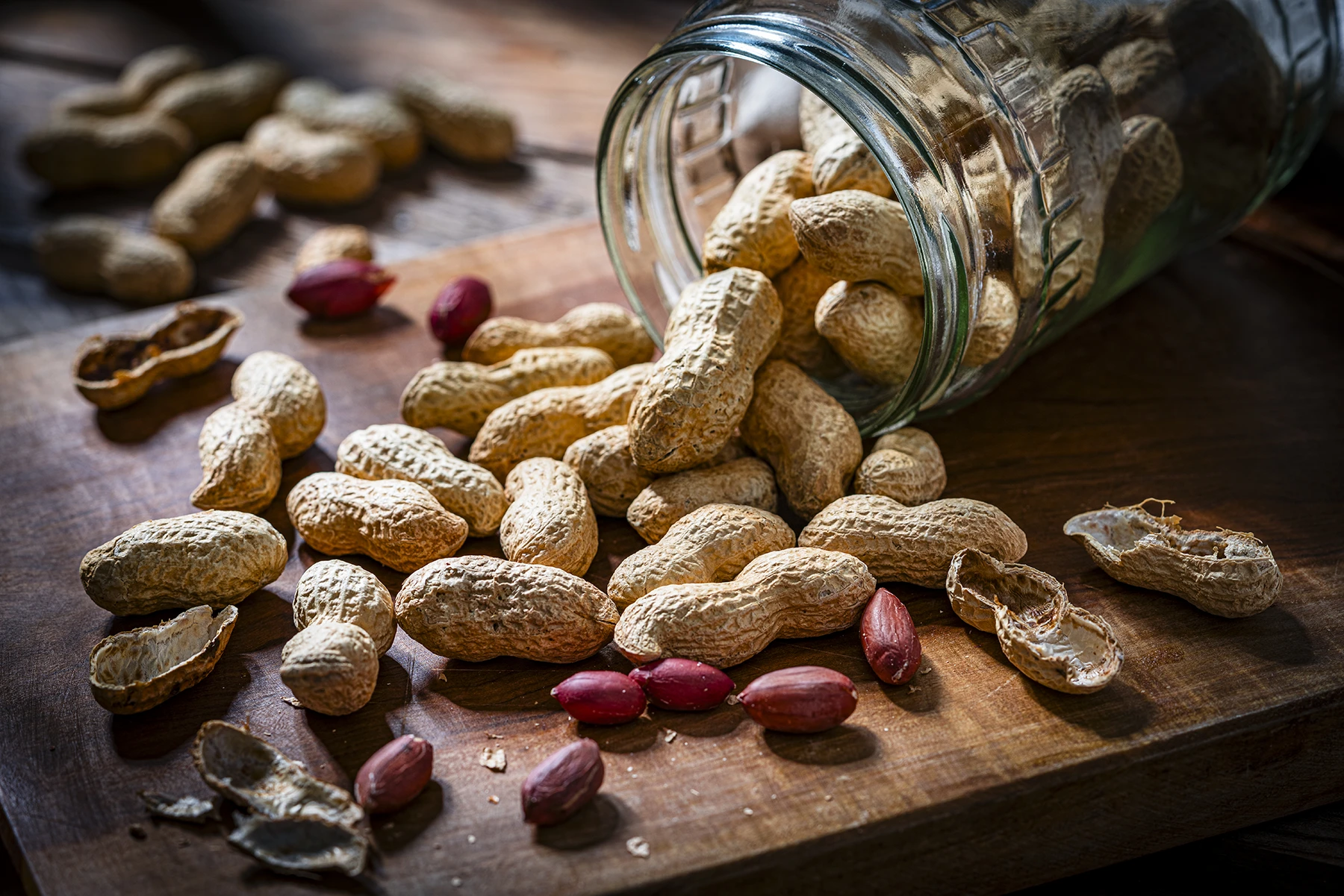 Peanuts flowing out of overturned glass jar.