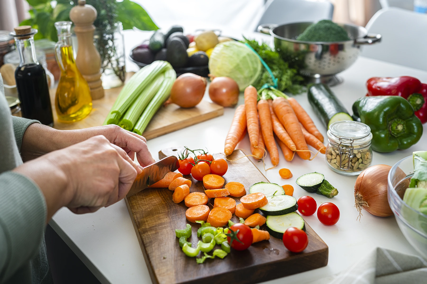 Close up of woman's hands slicing fresh organic carrots on kitchen counter - stock photo