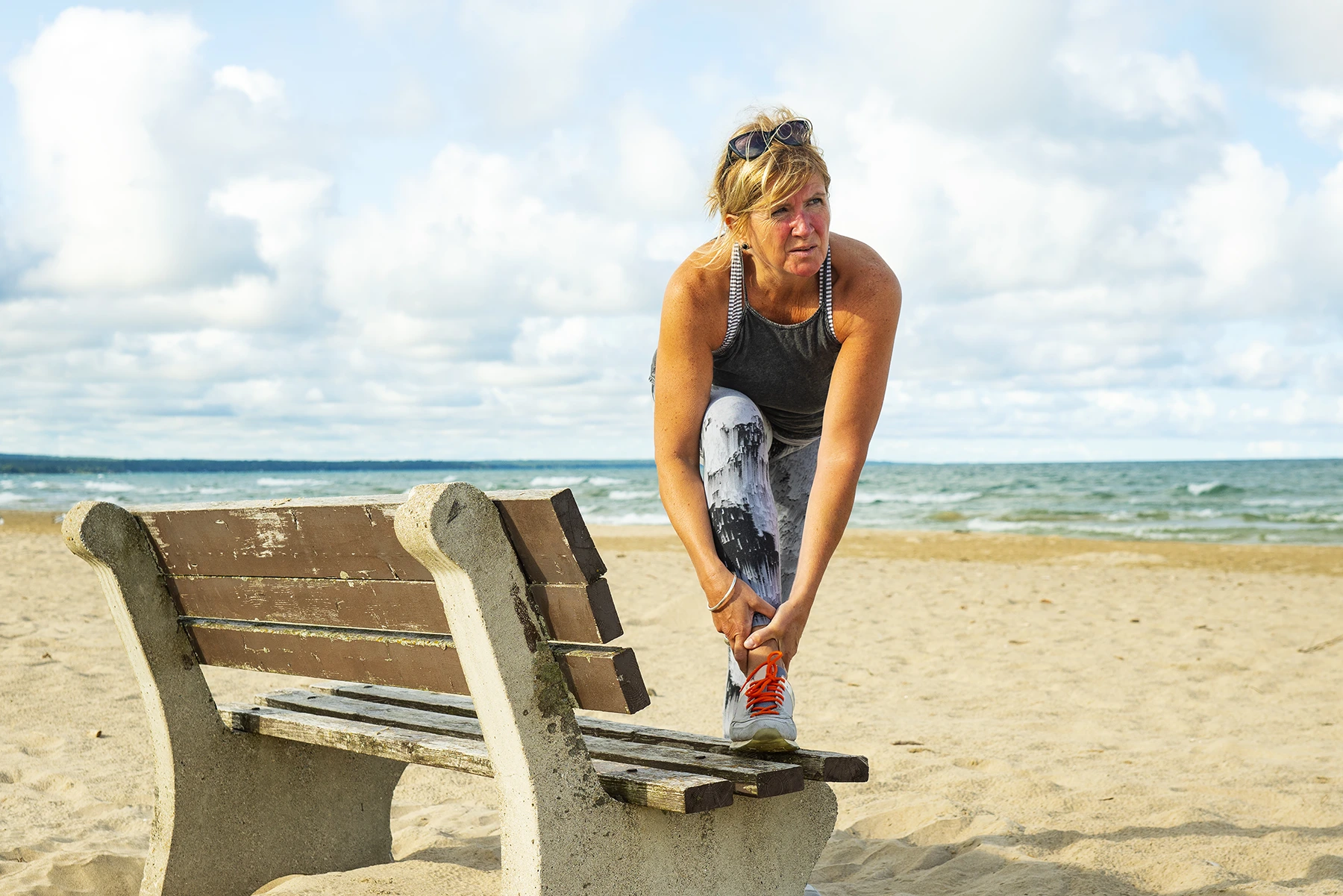 Female jogger stops at bench on beach. Massages her ACL.
