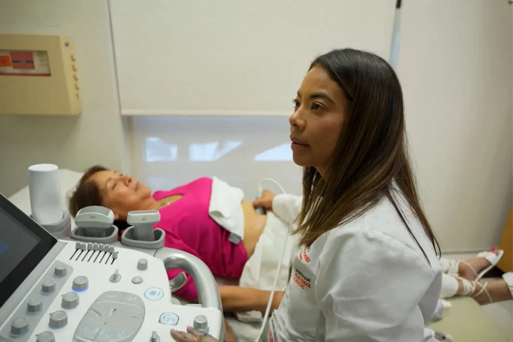 Sonographer performing an abdominal ultrasound on a female patient in a clinic.