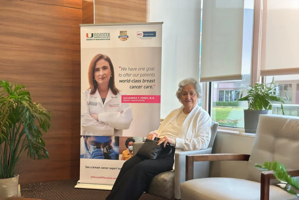 Dr. Perez's mother sits in front of a banner of Dr. Perez at Sylvester office.