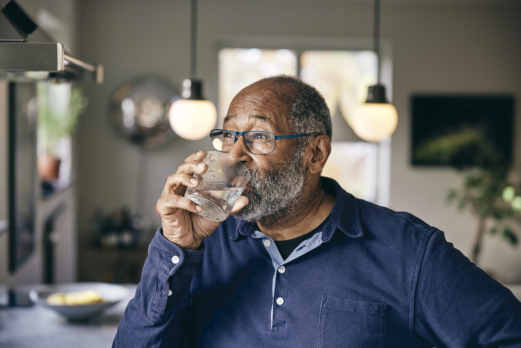 Contemplative senior man drinking water at home - stock photo