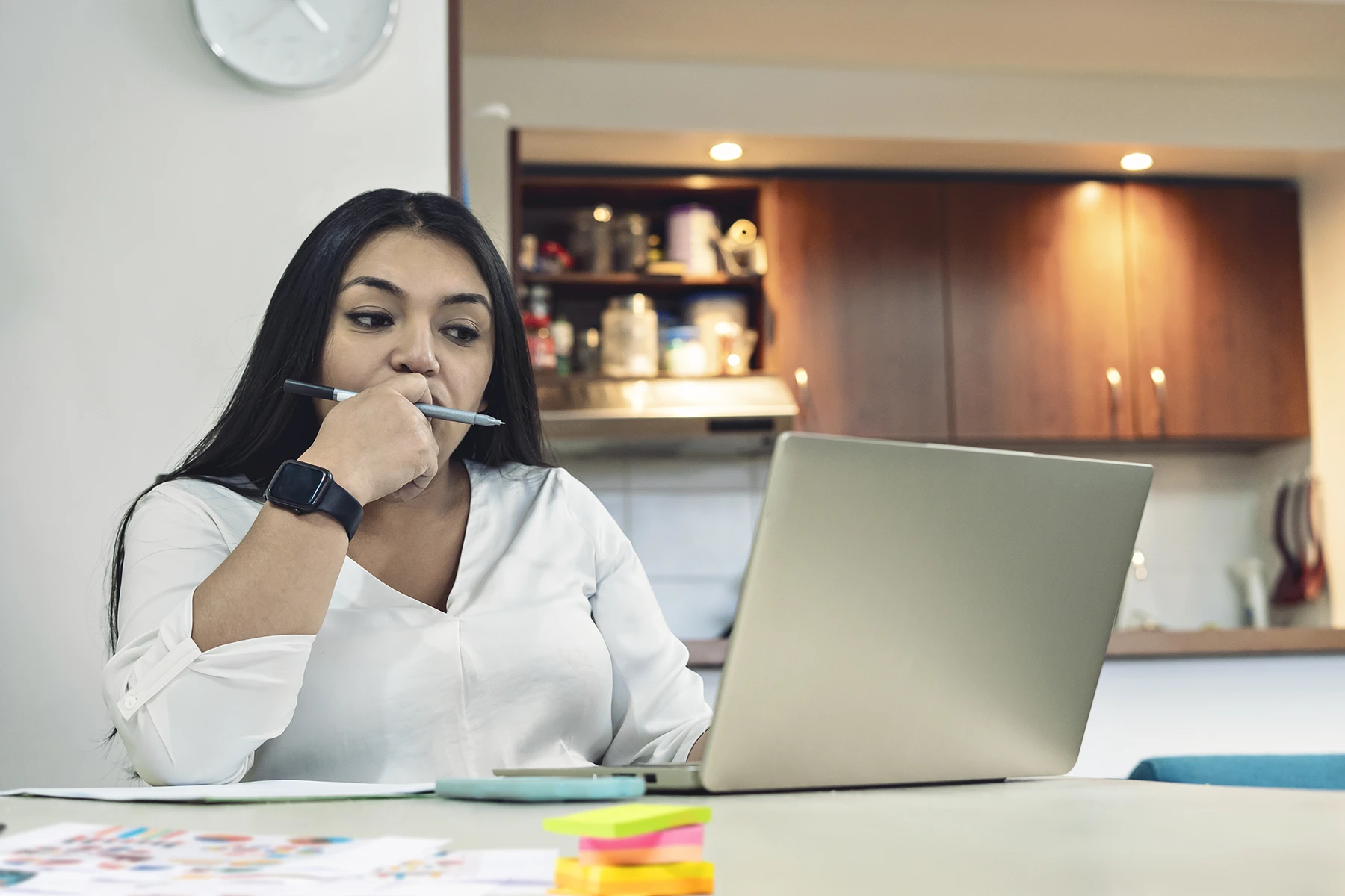Woman researching online with her laptop sitting in the dining room of her home. - stock photo