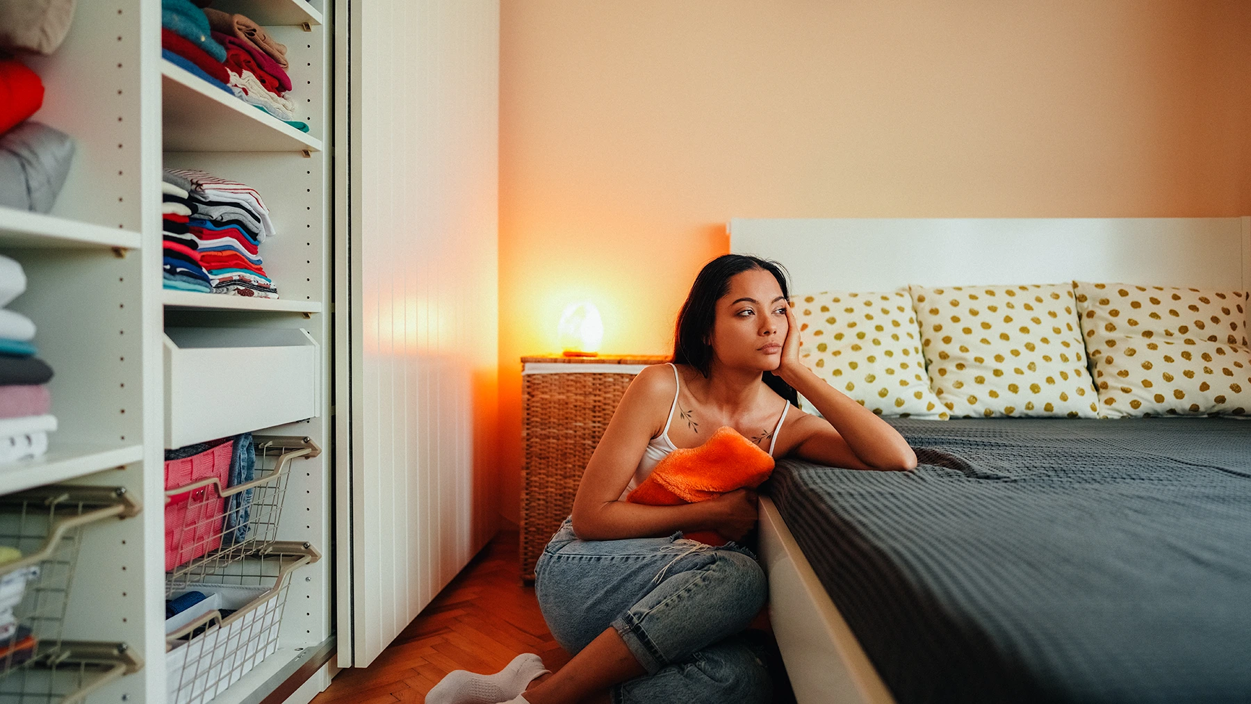 Woman with stomach pain from endometriosis staying home sits on floor at side of bed- stock photo