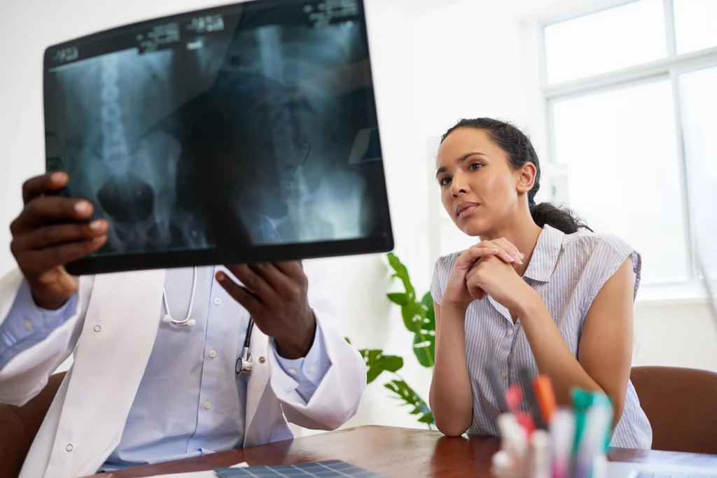 Male doctor explains spinal x-ray results to young worried woman in office - stock photo