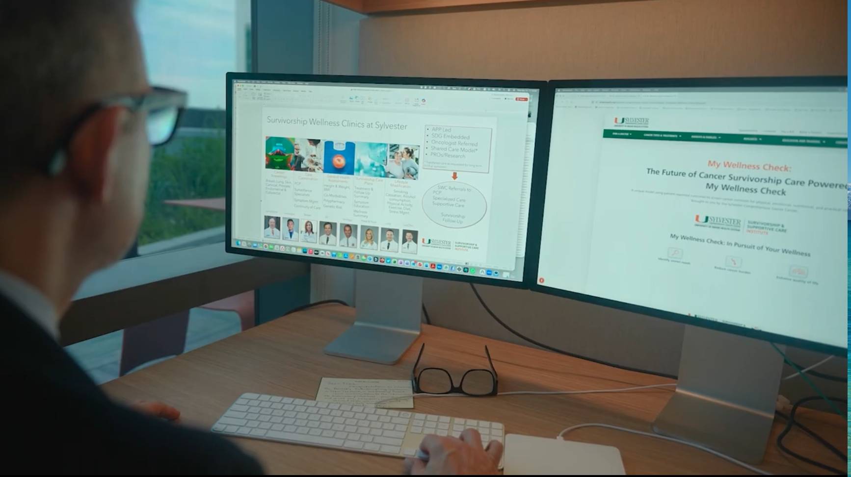 A professional, viewed from behind, works at a desk with dual monitors displaying information about "Survivorship Wellness Clinics at Sylvester" and a "My Wellness Check" website for cancer survivorship care.