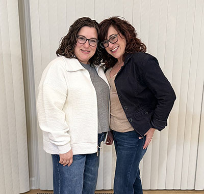 Rochelle Broder-Singer and her sister, Ilyse, standing together indoors.