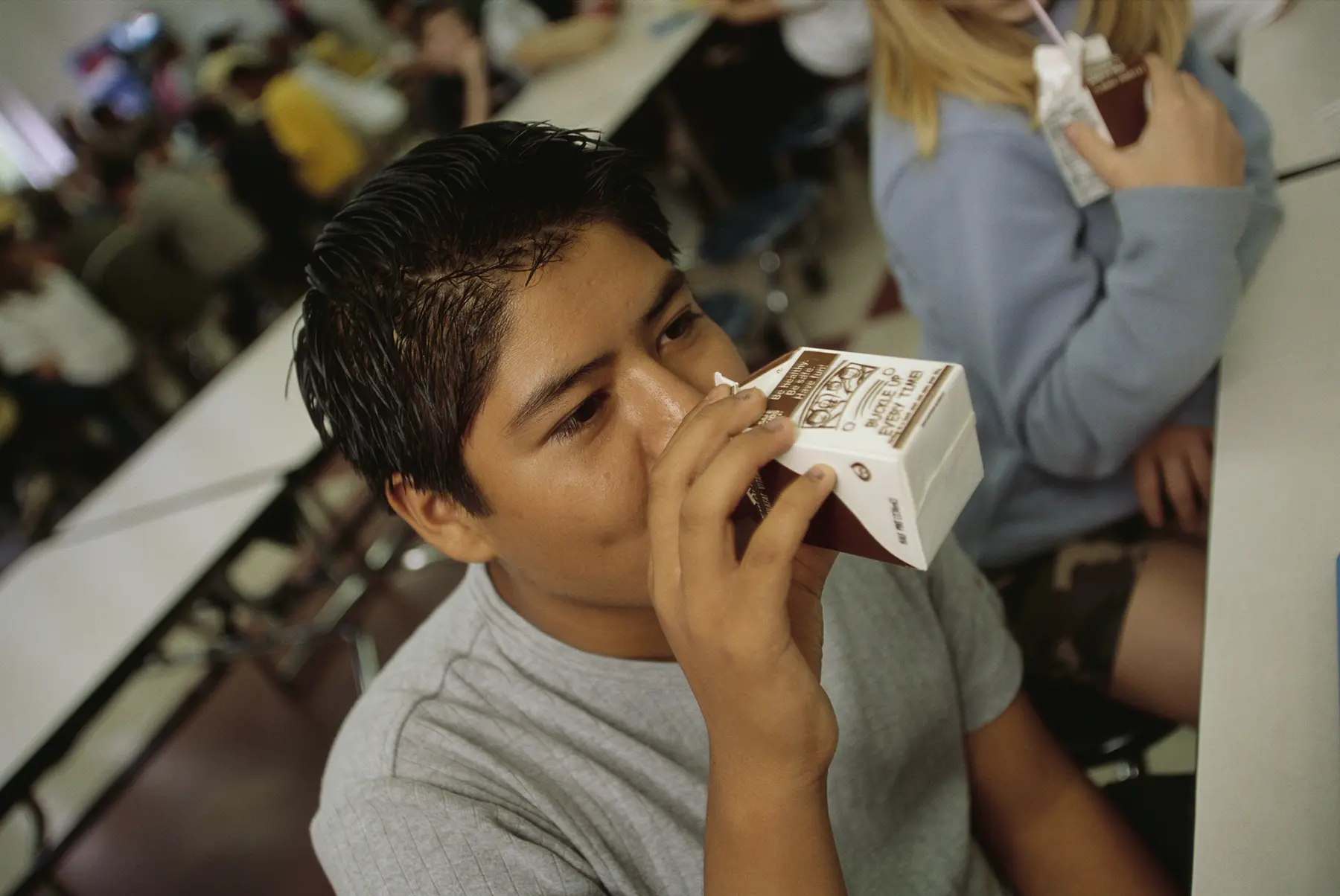 Hispanic teen drinks chocolate milk during his lunch break.