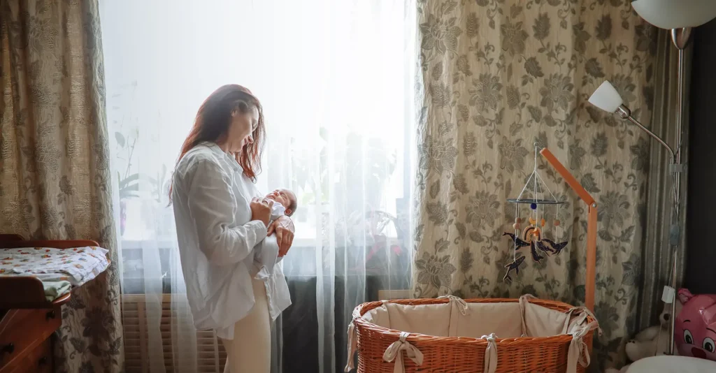 mom cuddling newborn daughter in home nursery setting