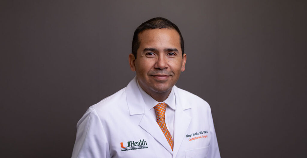 Dr. Diego Avella-Patino in white medical coat and red tie, sitting for a portrait photo